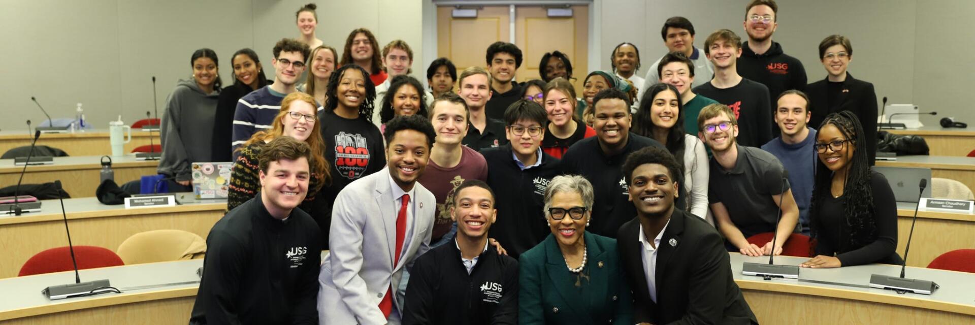 Group of students and Joyce Beatty standing and smiling in the Ohio Union Senate Chamber